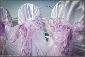 White chair covers with mauve bows make this wedding decor simple but elegant.