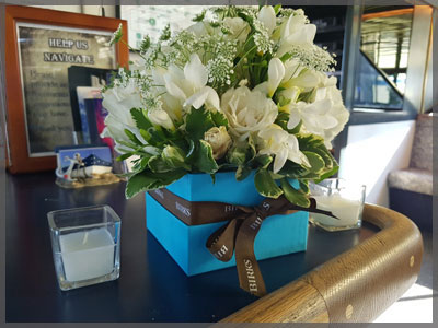 Centrepiece with white flowers in a blue square vase for a corporate cruise.