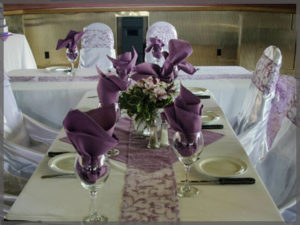 Table centrepiece with mauve napkins in wine glasses for a wedding cruise.