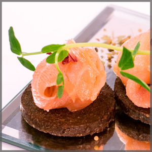 Hor D'oeuvres of salmon on a round pumpernickel wafer.