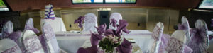 Wedding decor with white chair covers and lavender napkins and bows.