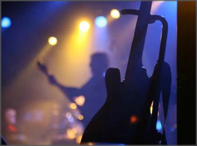 Live bands silhouette with guy playing guitar and electric guitar in the front right of the image.